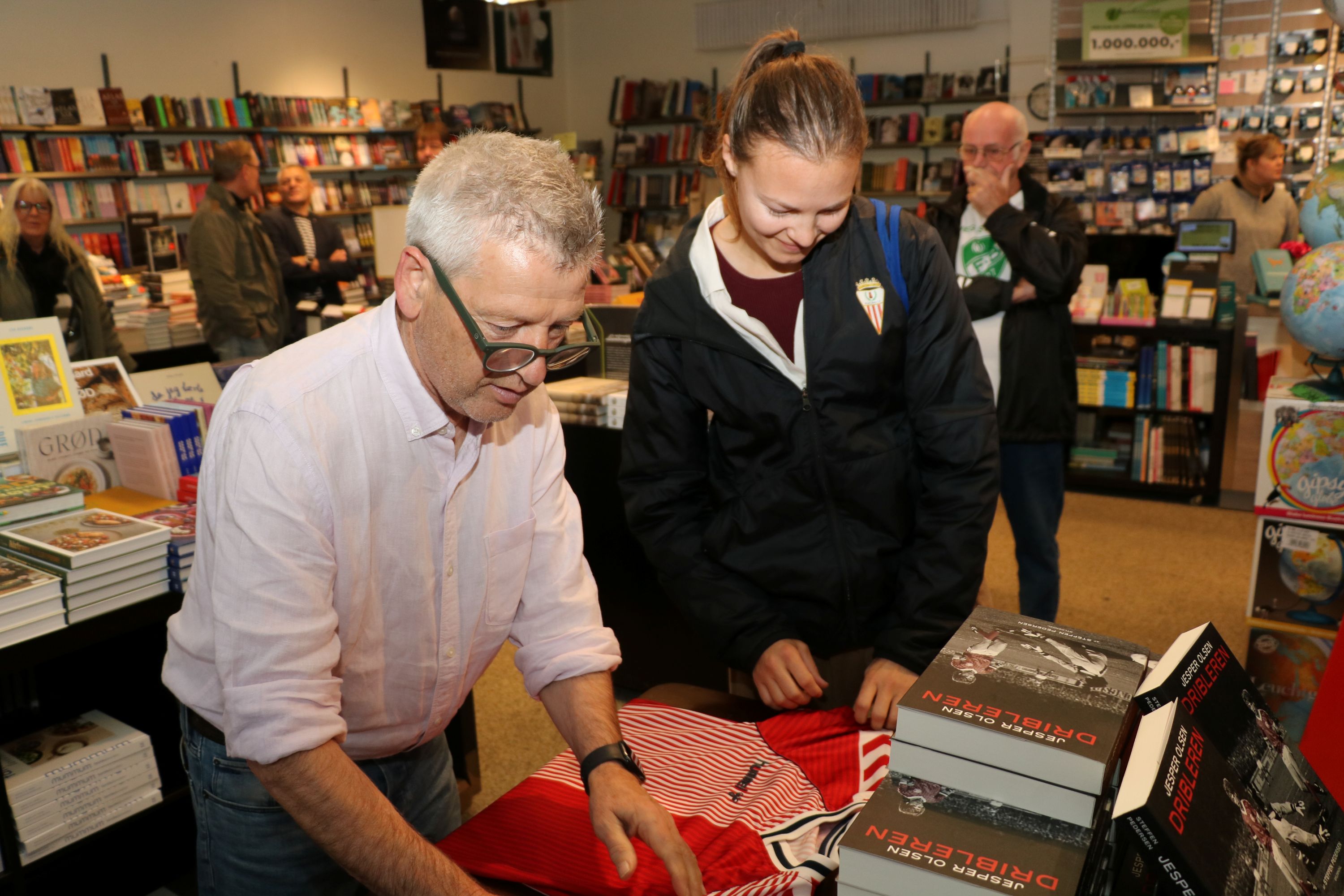 Omkring 100 mennesker var forbi Boghuset i Faxe lørdag for at hilse på Jesper Olsen og få en signatur - som her hvor en fan får autografen på landsholdstrøjen fra 1986 i Mexico. Foto: John Ringstrøm