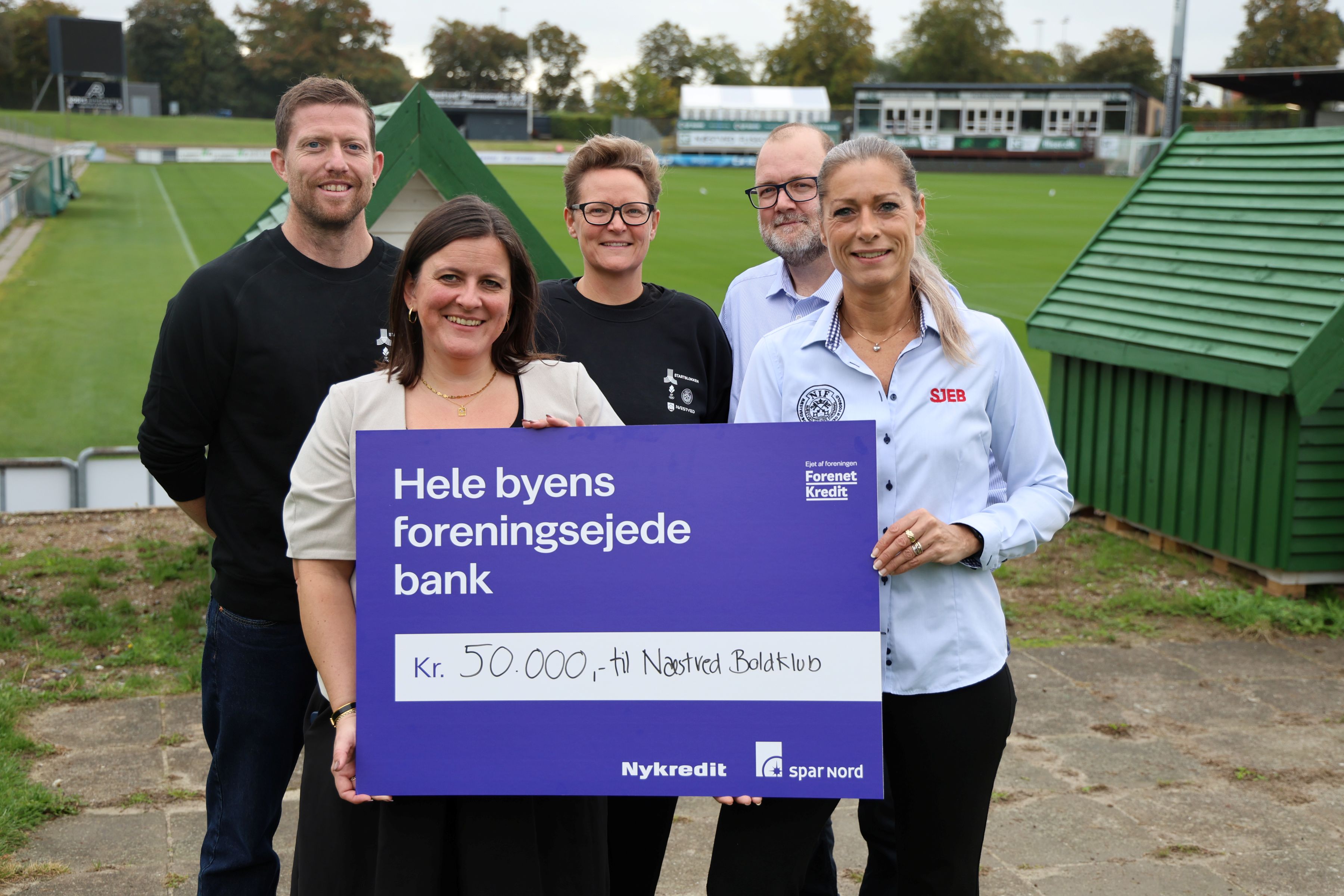 I sorte trøjer er det Tobias Nøhr Pedersen og Pernille Sidenius, der sammen med Næstved Boldklubs administrationschef Celine Knarreborg (th) glæder sig over donationen på de 50.000 kroner. Christina Birk Batsberg og Jonas Danielsson fra Nykredit Spar Nord overrækker checken. Foto: John Ringstrøm